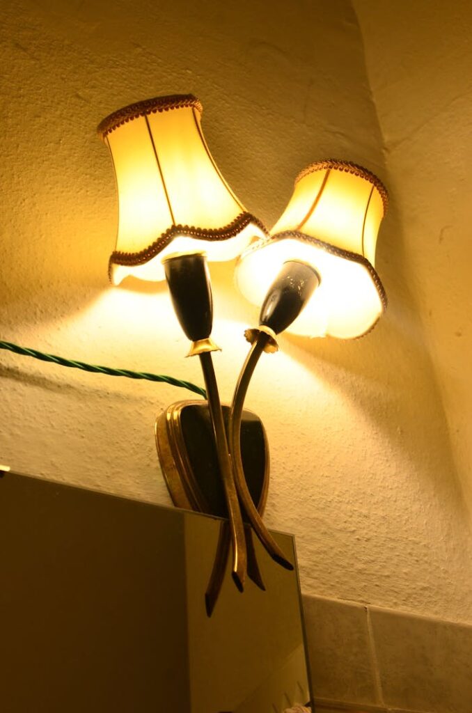 From below of sconce with bright shiny lamps hanging on rough wall with wire in dark room in evening time